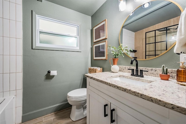 bathroom with a textured wall, toilet, a washtub, wood finished floors, and vanity