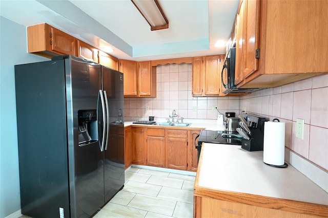 kitchen with brown cabinets, black appliances, a tray ceiling, backsplash, and light countertops