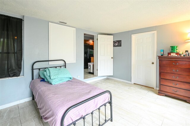 bedroom featuring visible vents, baseboards, a textured ceiling, and black refrigerator with ice dispenser