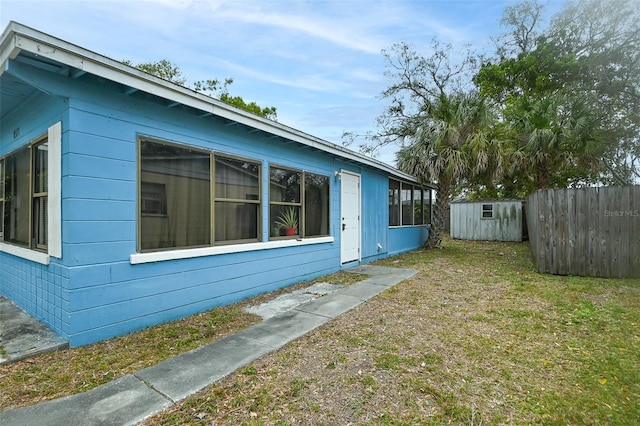 view of home's exterior with a yard, an outbuilding, a storage shed, and fence