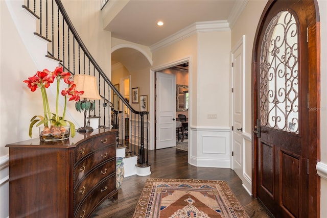 entryway with arched walkways, a wainscoted wall, crown molding, dark wood finished floors, and a decorative wall