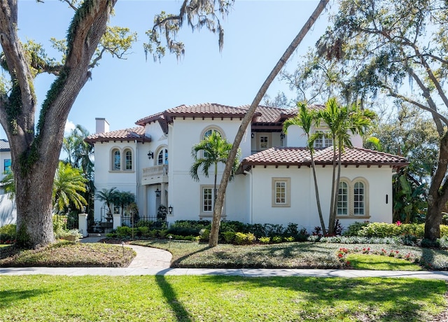 mediterranean / spanish-style house with a tiled roof, a front lawn, a chimney, and stucco siding