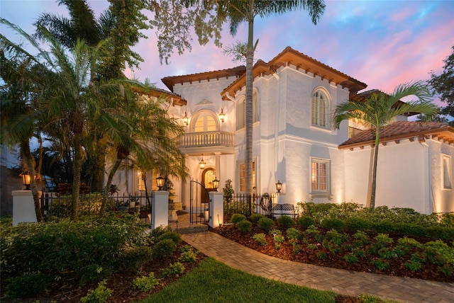 mediterranean / spanish-style home featuring a balcony, a fenced front yard, a gate, and stucco siding