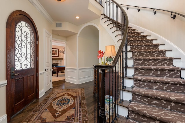 entryway with crown molding, visible vents, a decorative wall, wainscoting, and wood finished floors