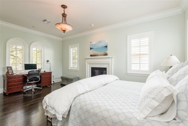 bedroom with baseboards, visible vents, a glass covered fireplace, dark wood-style floors, and crown molding