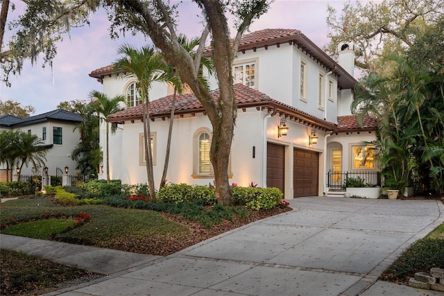 mediterranean / spanish-style home with a chimney, driveway, a tiled roof, and stucco siding