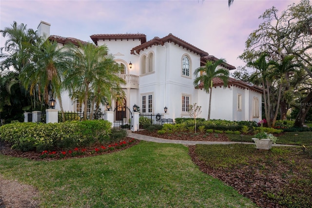 mediterranean / spanish-style home featuring a balcony, stucco siding, a fenced front yard, a gate, and a front yard