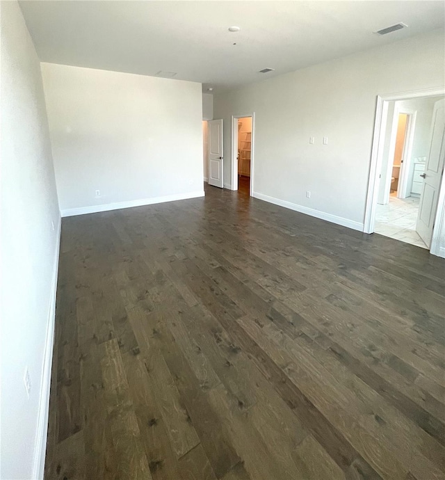 spare room featuring dark wood-type flooring, visible vents, and baseboards