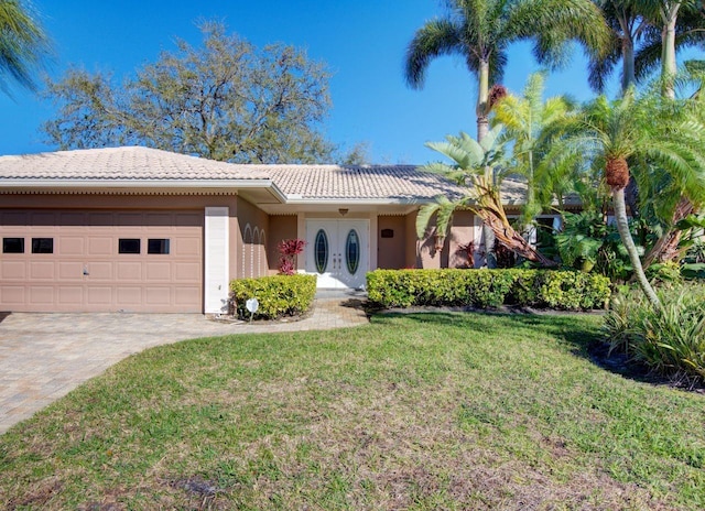 ranch-style house featuring a tile roof, an attached garage, decorative driveway, french doors, and a front yard