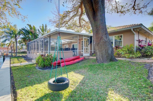 rear view of property featuring stucco siding, glass enclosure, and a yard