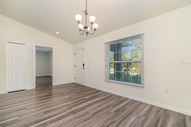 empty room featuring lofted ceiling, a notable chandelier, baseboards, and wood finished floors