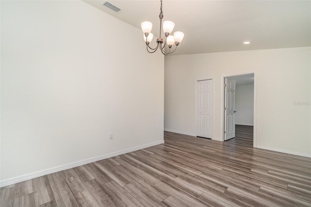 unfurnished room featuring a chandelier, wood finished floors, visible vents, and baseboards