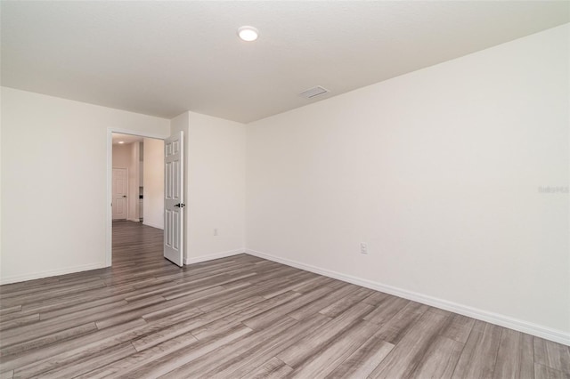 spare room featuring wood finished floors, visible vents, and baseboards