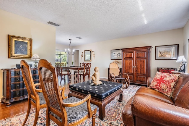 living room with a textured ceiling, light wood-type flooring, visible vents, and a notable chandelier