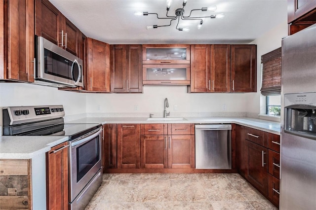 kitchen with appliances with stainless steel finishes, light countertops, a sink, and glass insert cabinets