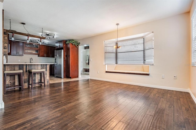 unfurnished living room featuring dark wood-style flooring, a sink, and baseboards