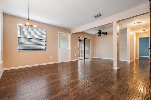 empty room featuring dark wood-style flooring, visible vents, baseboards, and ceiling fan with notable chandelier