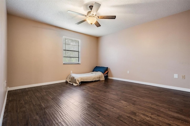 unfurnished bedroom with dark wood-type flooring, a textured ceiling, baseboards, and a ceiling fan