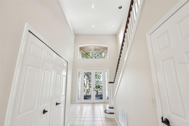 entrance foyer with light tile patterned floors, a towering ceiling, visible vents, stairs, and french doors