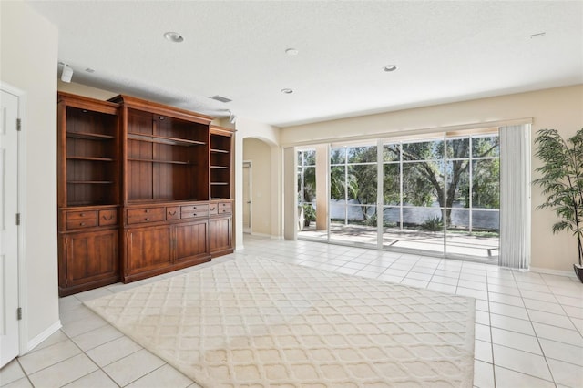 unfurnished living room with arched walkways, light tile patterned flooring, visible vents, and baseboards