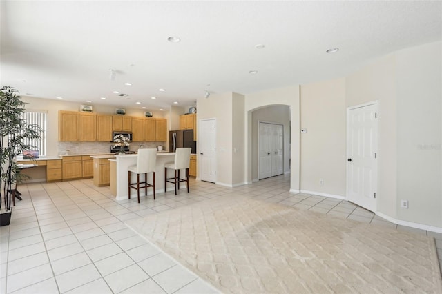 kitchen with arched walkways, light tile patterned floors, stainless steel appliances, light countertops, and backsplash