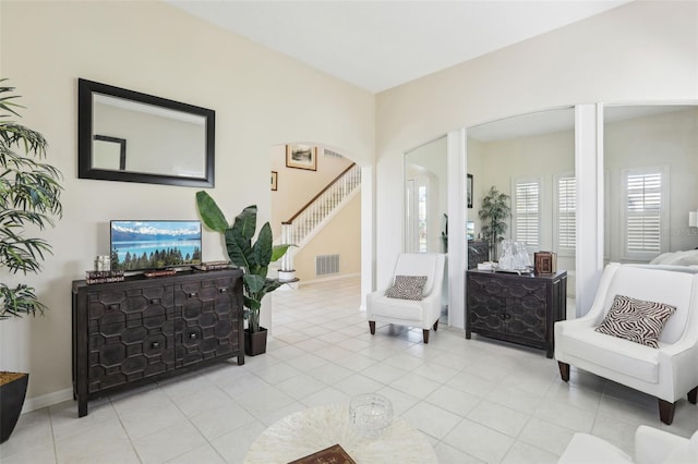 living area with arched walkways, light tile patterned floors, stairway, and visible vents
