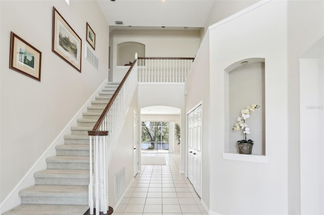 stairs featuring tile patterned flooring, a towering ceiling, and baseboards