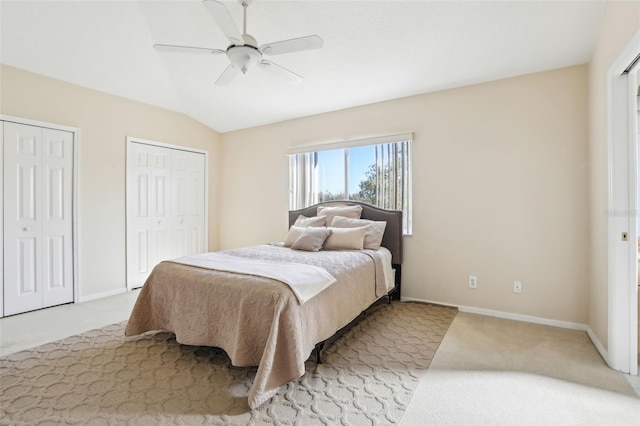 carpeted bedroom with a ceiling fan, lofted ceiling, baseboards, and two closets
