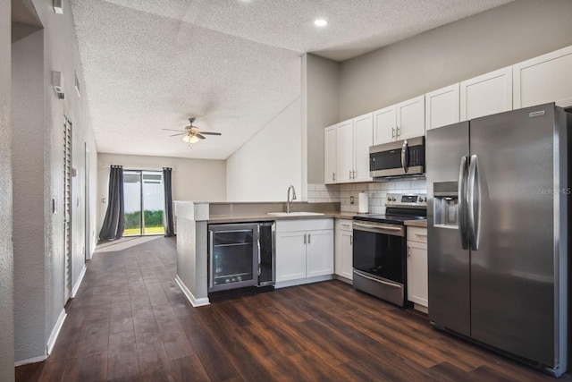 kitchen with a peninsula, beverage cooler, appliances with stainless steel finishes, and white cabinets