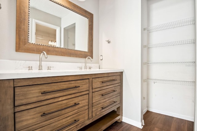 full bath with double vanity, wood finished floors, a sink, and baseboards