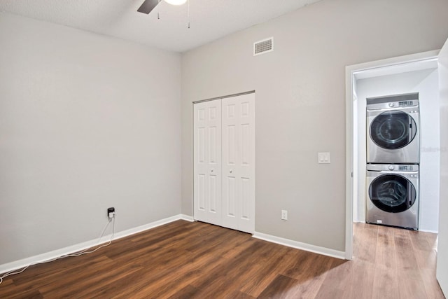 clothes washing area with stacked washer and dryer, laundry area, visible vents, baseboards, and dark wood finished floors