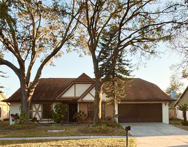 english style home with an attached garage, brick siding, concrete driveway, and stucco siding