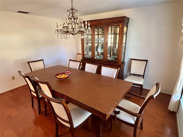 dining space with a textured ceiling, wood finished floors, visible vents, and baseboards