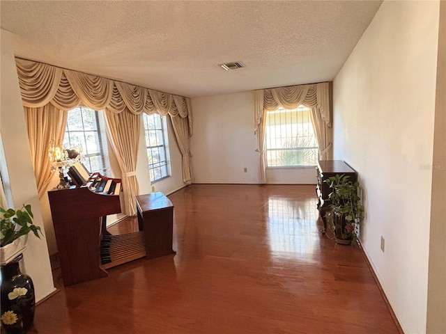 interior space with visible vents, a textured ceiling, baseboards, and wood finished floors