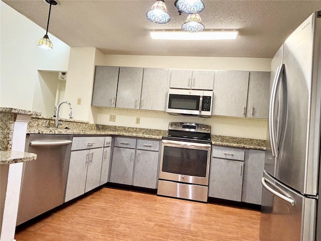 kitchen with a textured ceiling, appliances with stainless steel finishes, gray cabinets, and light wood-style flooring