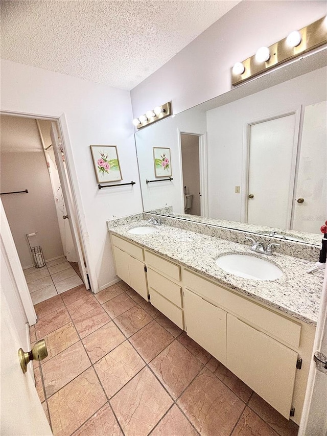 full bath featuring double vanity, a textured ceiling, and a sink