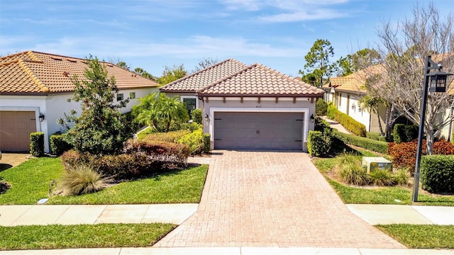 mediterranean / spanish house with decorative driveway, a tiled roof, an attached garage, and stucco siding