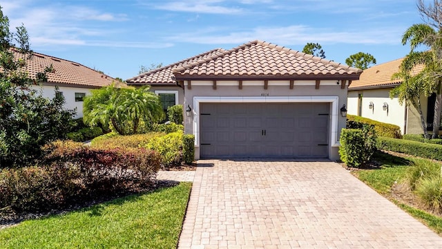 mediterranean / spanish house with decorative driveway, a tile roof, an attached garage, and stucco siding