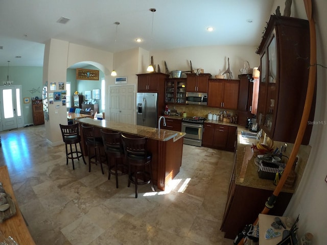 kitchen with arched walkways, tasteful backsplash, visible vents, appliances with stainless steel finishes, and glass insert cabinets