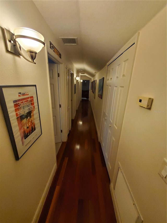 hall with dark wood-style flooring, visible vents, and baseboards