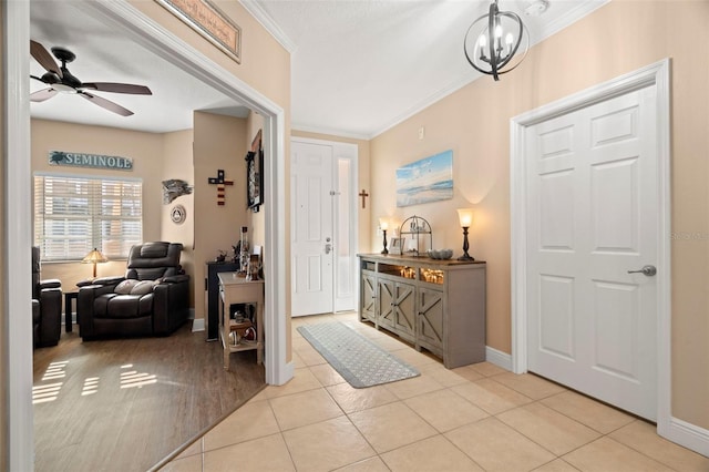 foyer with ornamental molding, ceiling fan with notable chandelier, baseboards, and light tile patterned floors