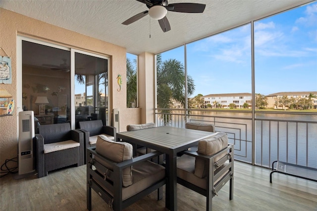 sunroom / solarium featuring a water view, plenty of natural light, and a ceiling fan