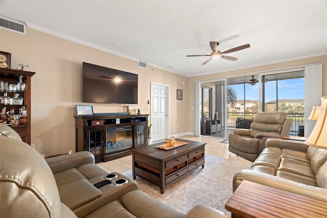 living area with a ceiling fan, a glass covered fireplace, visible vents, and crown molding