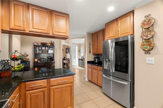 kitchen with light tile patterned floors, brown cabinetry, dark stone counters, range, and stainless steel fridge with ice dispenser