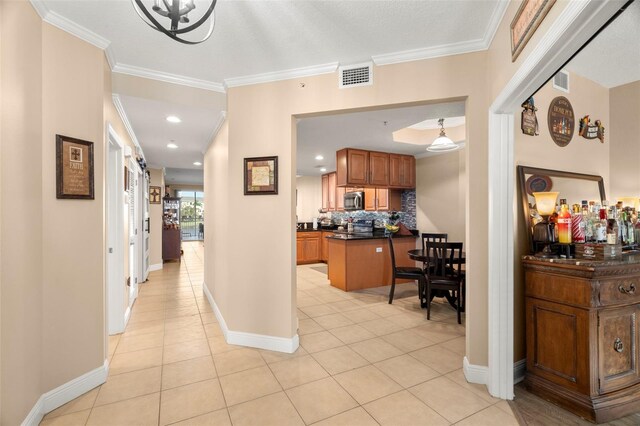 corridor featuring light tile patterned floors, ornamental molding, visible vents, and baseboards