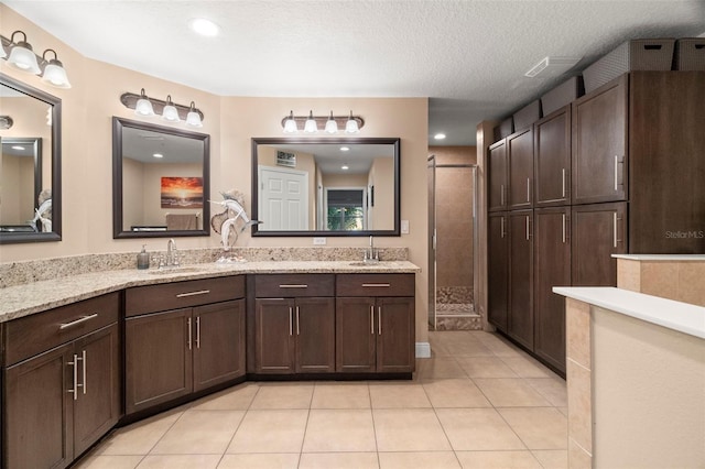 full bathroom featuring a textured ceiling, tile patterned flooring, a sink, a tile shower, and double vanity