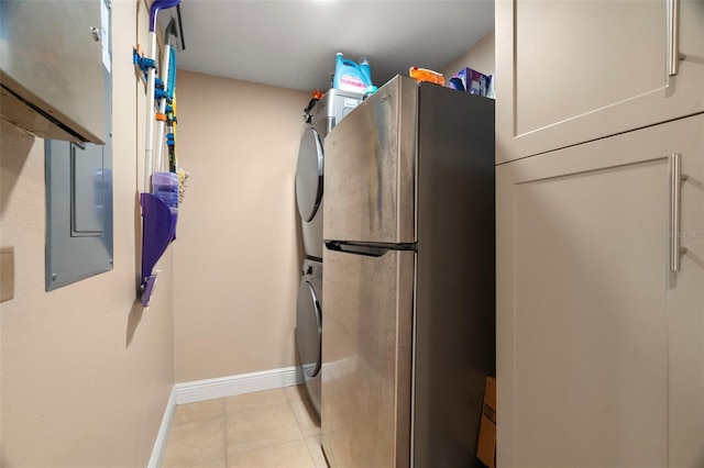 washroom featuring laundry area, stacked washer and clothes dryer, baseboards, and light tile patterned floors