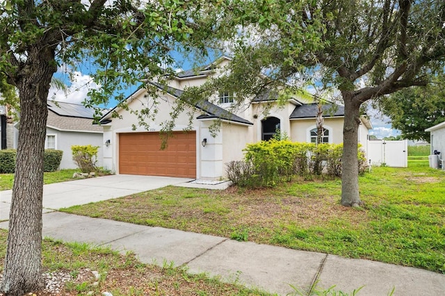 view of front facade featuring an attached garage, concrete driveway, a gate, stucco siding, and a front yard