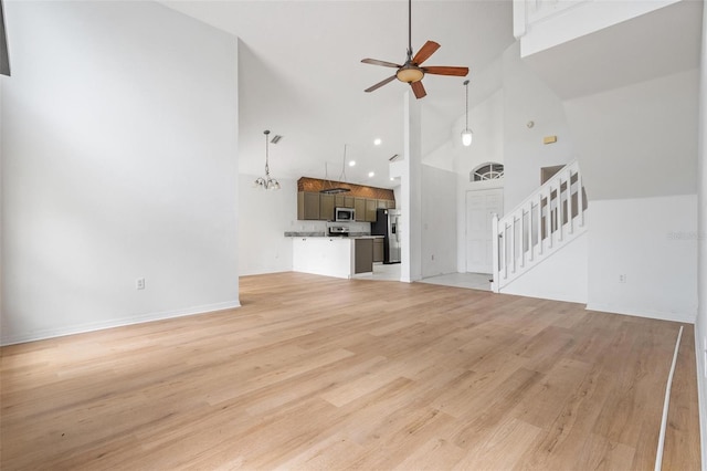 unfurnished living room with stairs, a towering ceiling, light wood-style flooring, and a ceiling fan