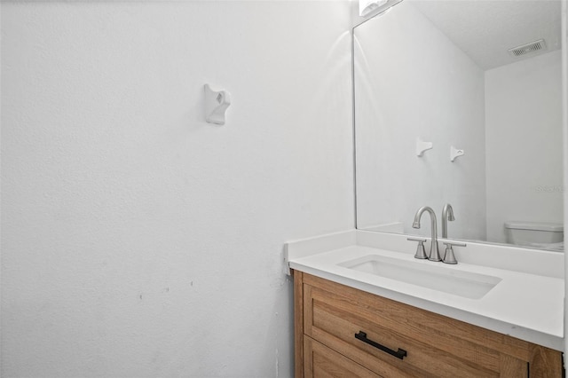 bathroom featuring toilet, vanity, and visible vents